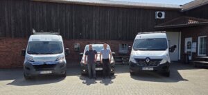 Zwei Männer stehen vor drei weißen Autos. Die Autos sind beklebt mit dem Logo von Grossmann & Hünken