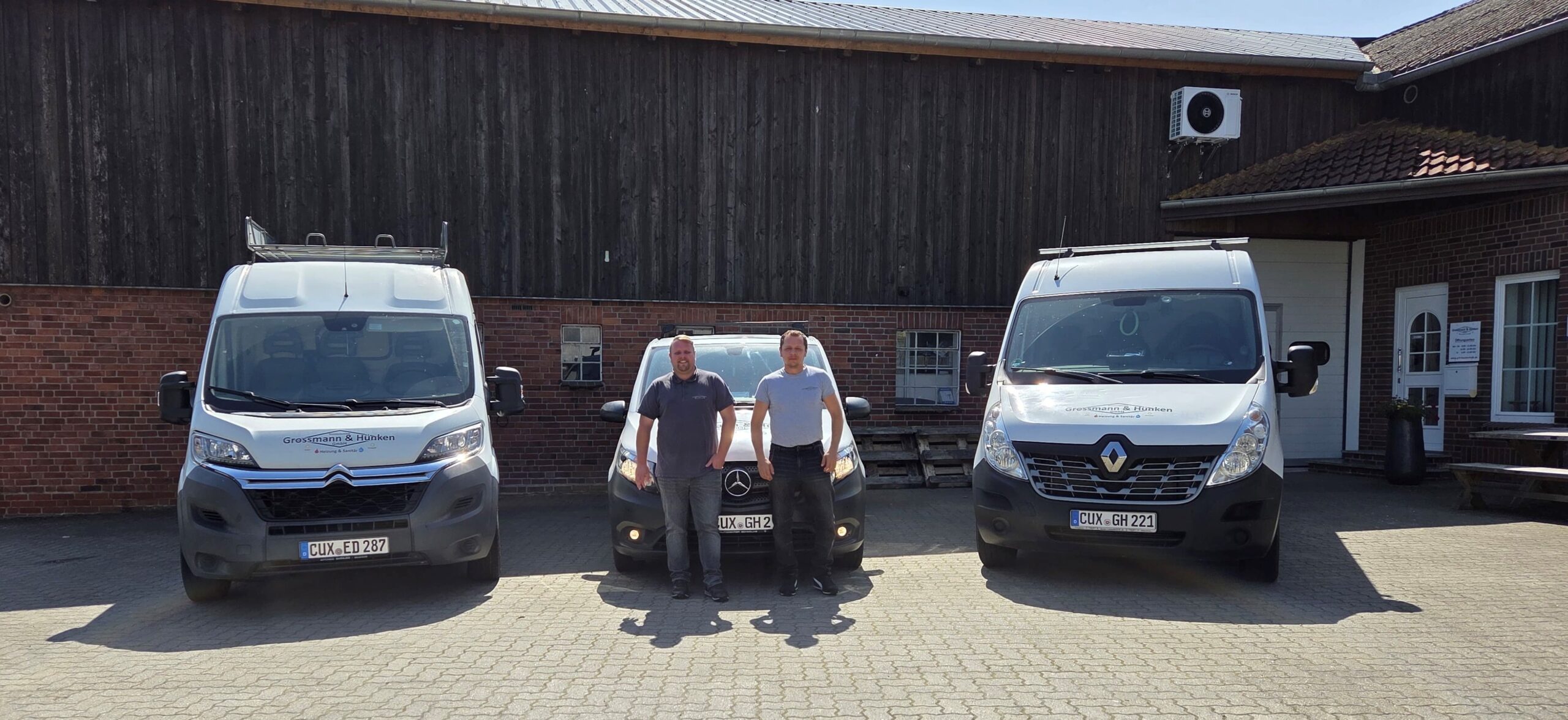 Zwei Männer stehen vor drei weißen Autos. Die Autos sind beklebt mit dem Logo von Grossmann & Hünken