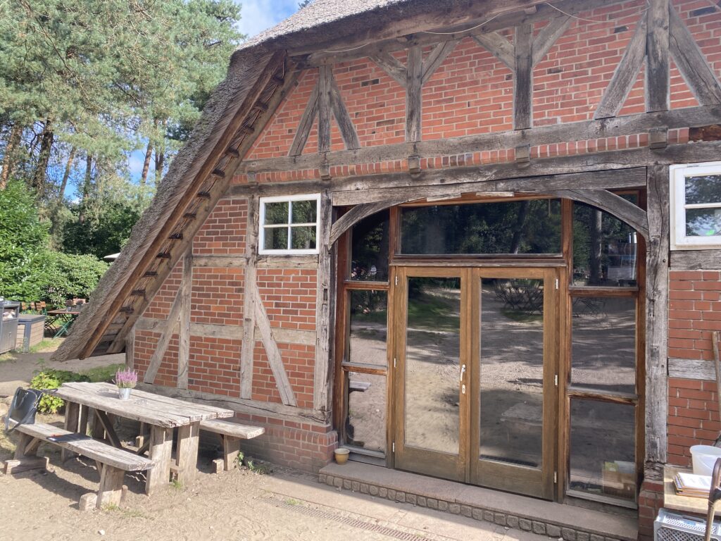 Das Restaurant Schafstall. Ein altes Fachwerkhaus und eine große gläserne Tür. Vor dem Haus stehen zwei Bänke und ein Tisch.