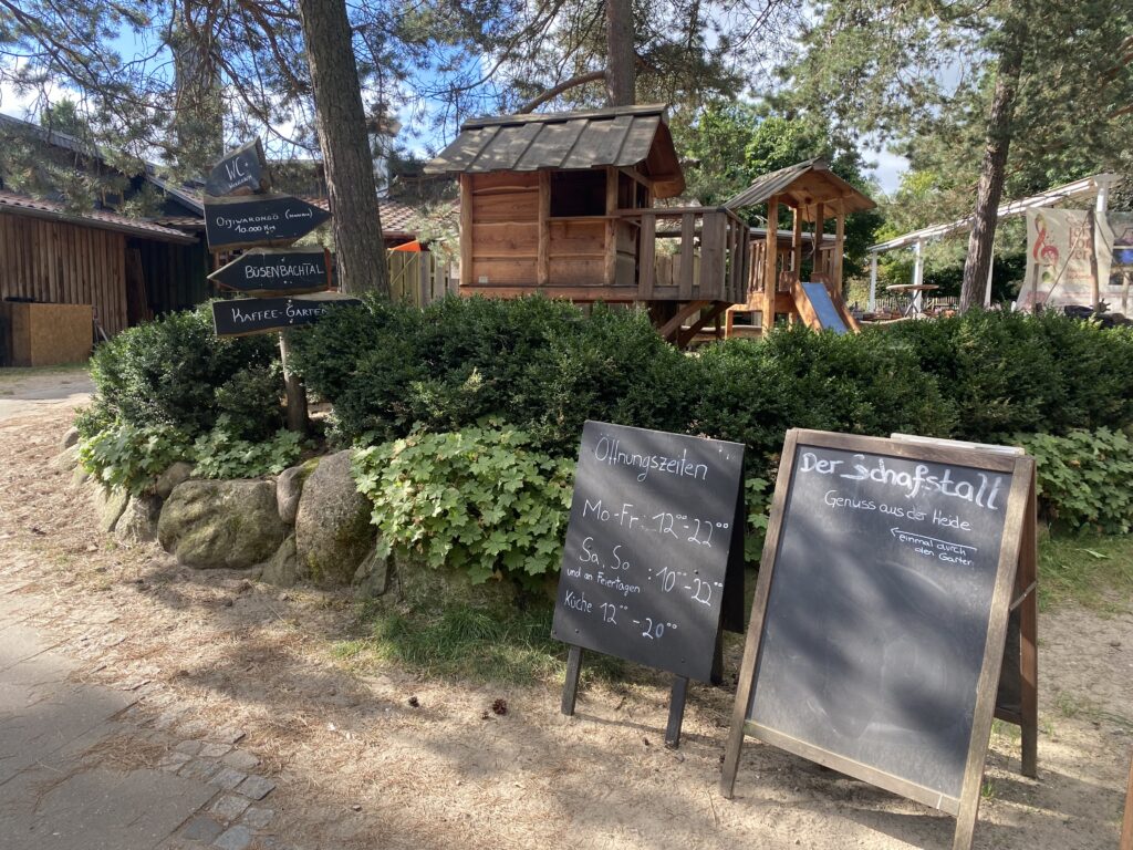 Kreidetafeln auf denen die Öffnungszeiten des Restaurants stehen und ein Kinderspielplatz im Hintergrund.